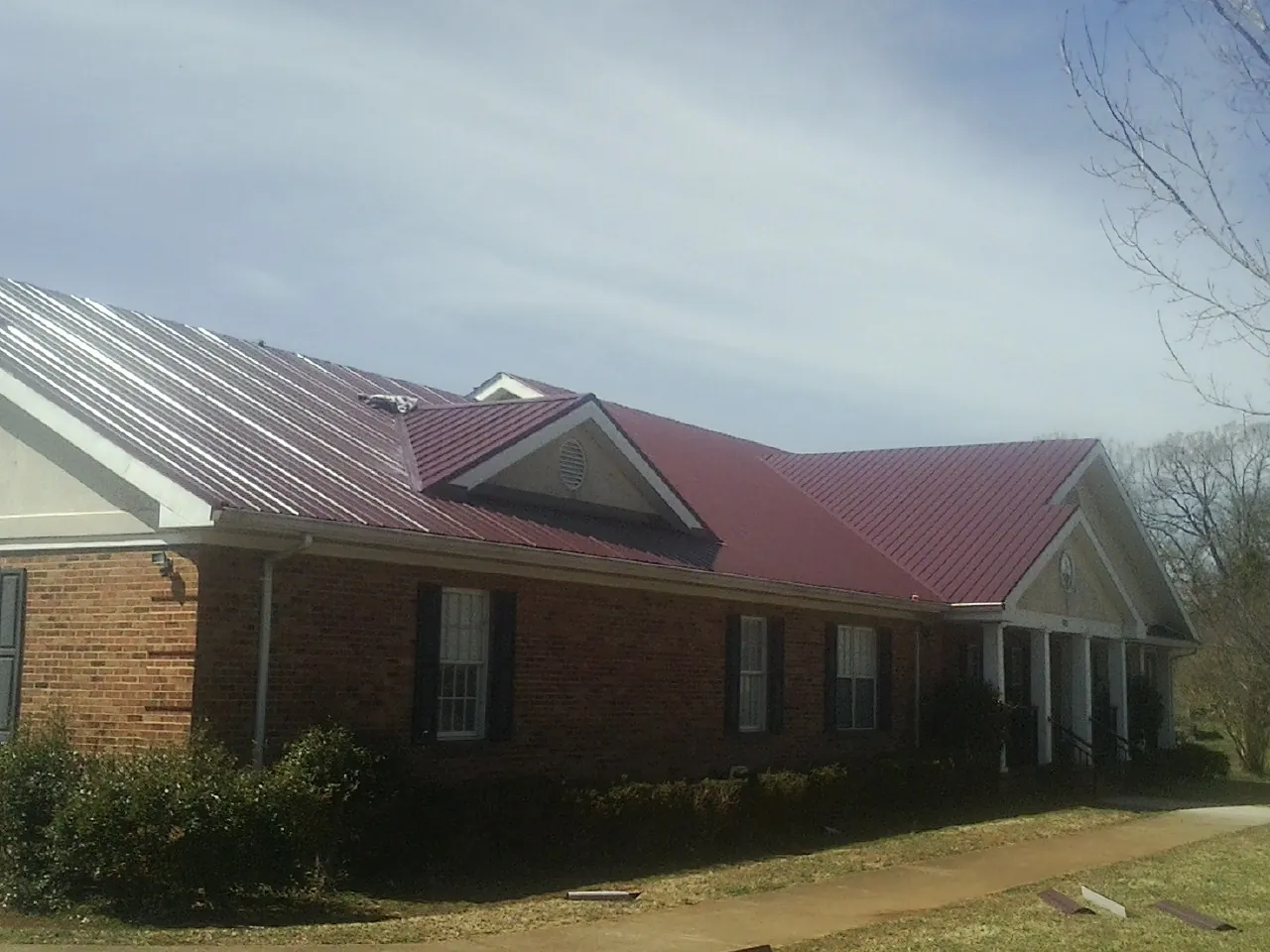 Red metal roof with gabled entries on a long brick building, from a Hail Damage Roof Repair job in Encinitas