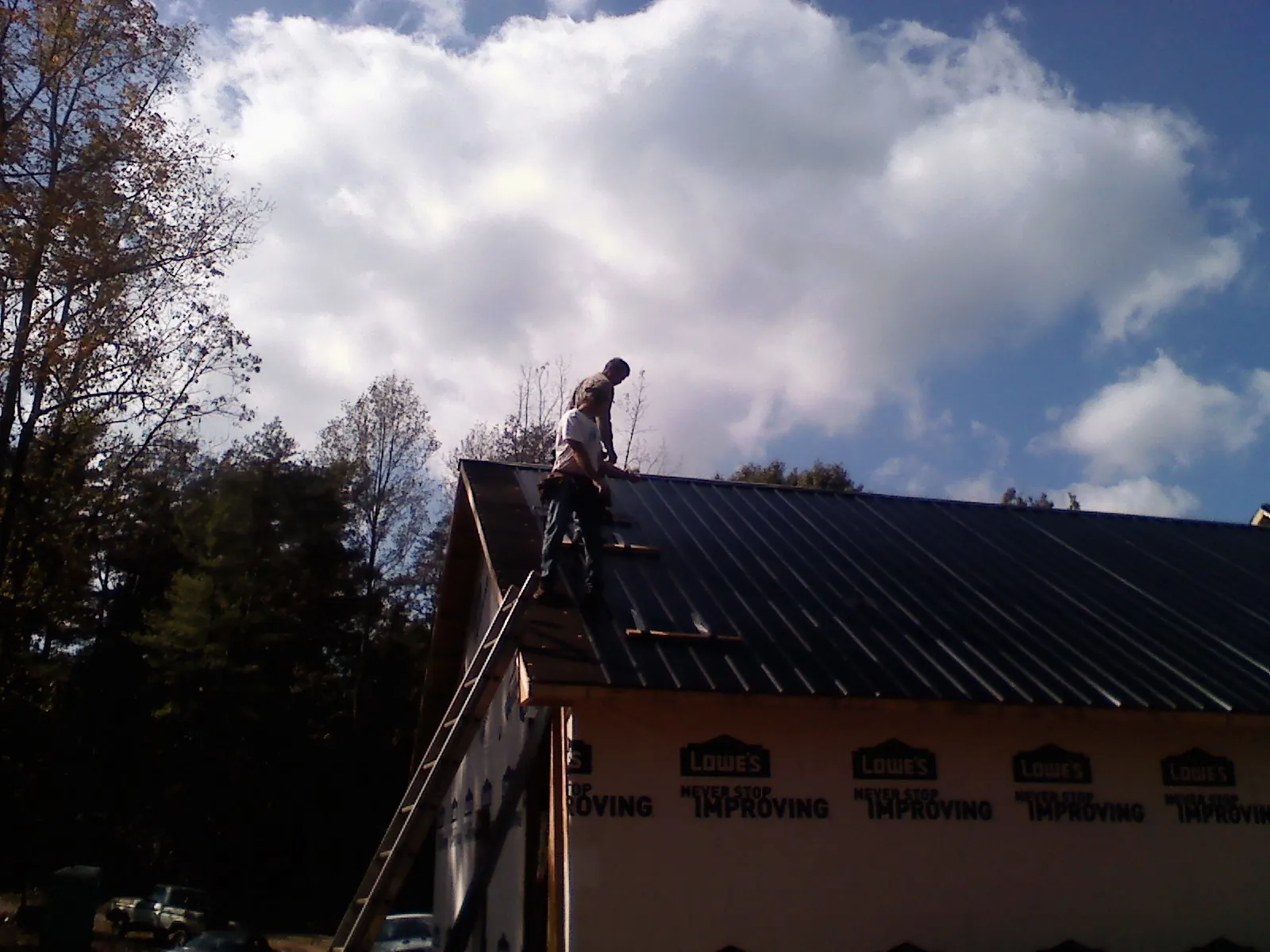 Roofer fastening dark metal panels high against a cloudy sky, from a Roof Inspection job in Encinitas