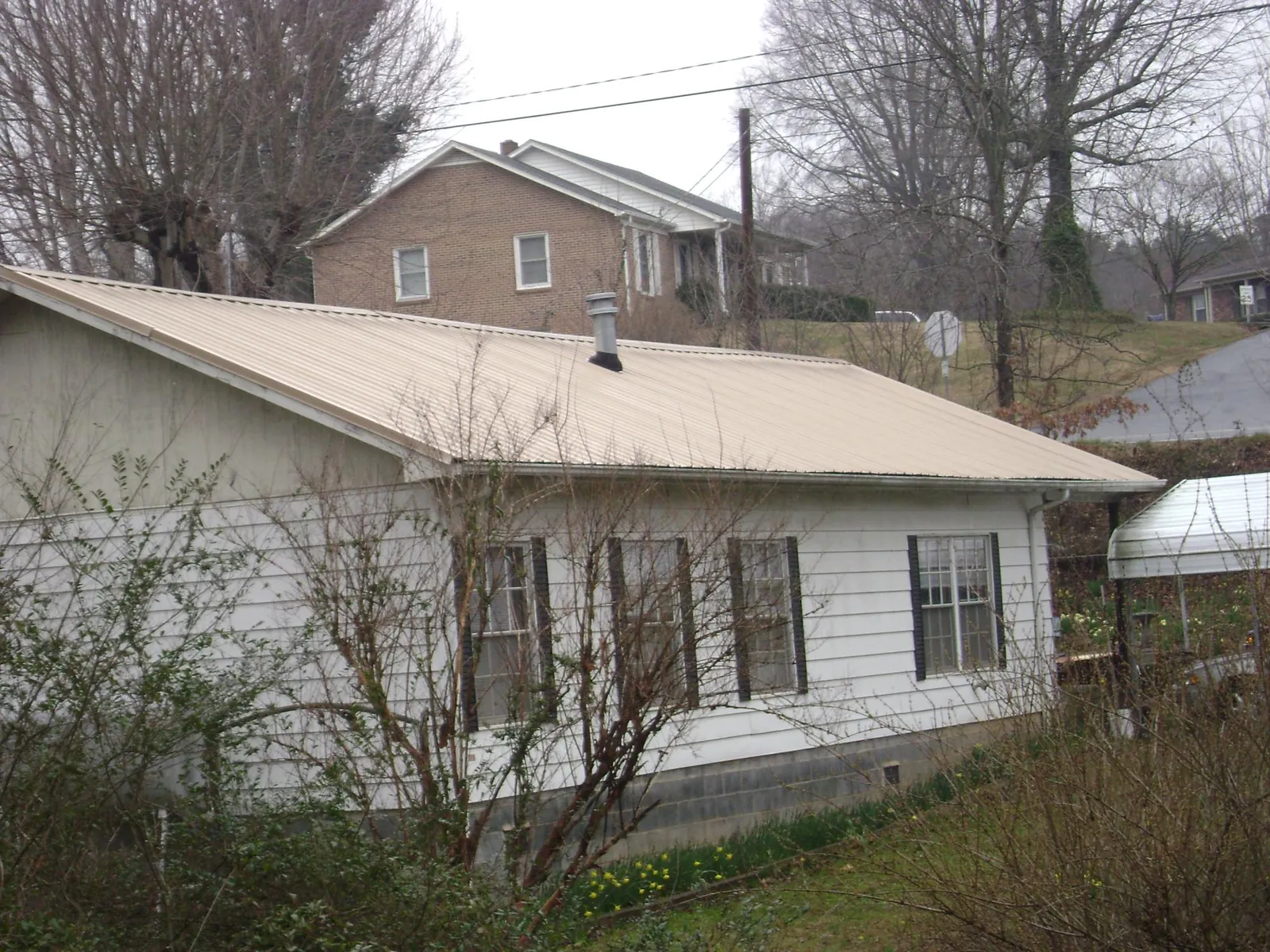 Tan metal roof on a white sided house set into a hillside — Commercial Roofing by Roofing Brothers in Encinitas